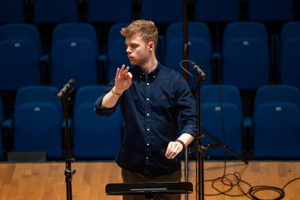 Adam Whitmore conducting in a concert hall with microphone stands
