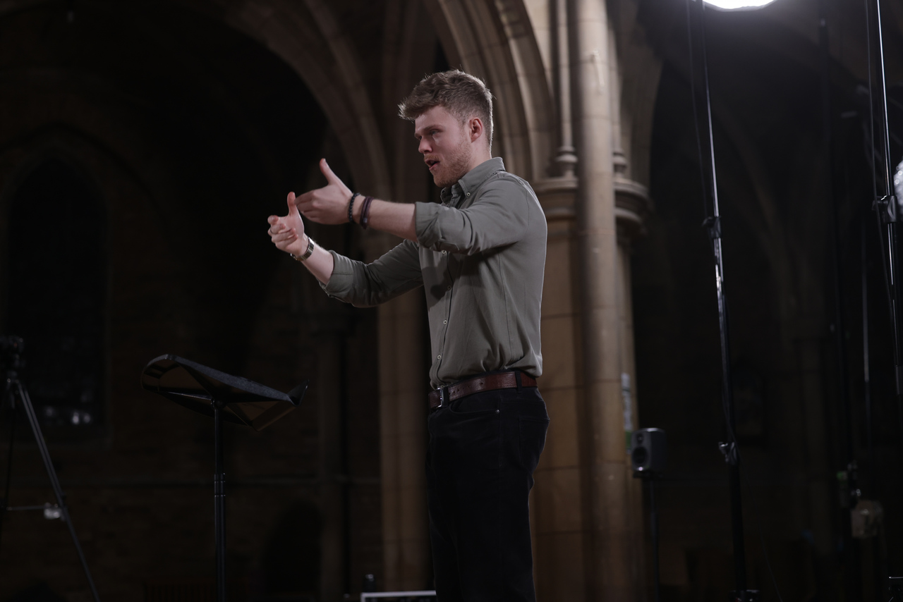 Adam Whitmore conducting with expressive hand gestures in a cathedral